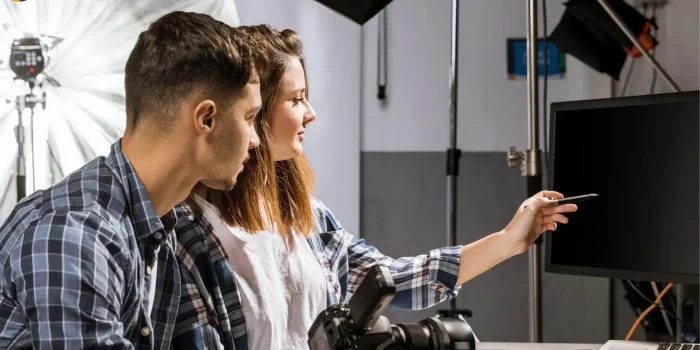 Two photographers reviewing photos on computer monitor in professional studio with lighting equipment and camera gear